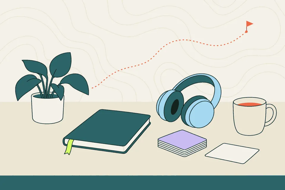A quiet desk with headphones, a notebook, a cup of tea and a short stack of cards with one set aside.